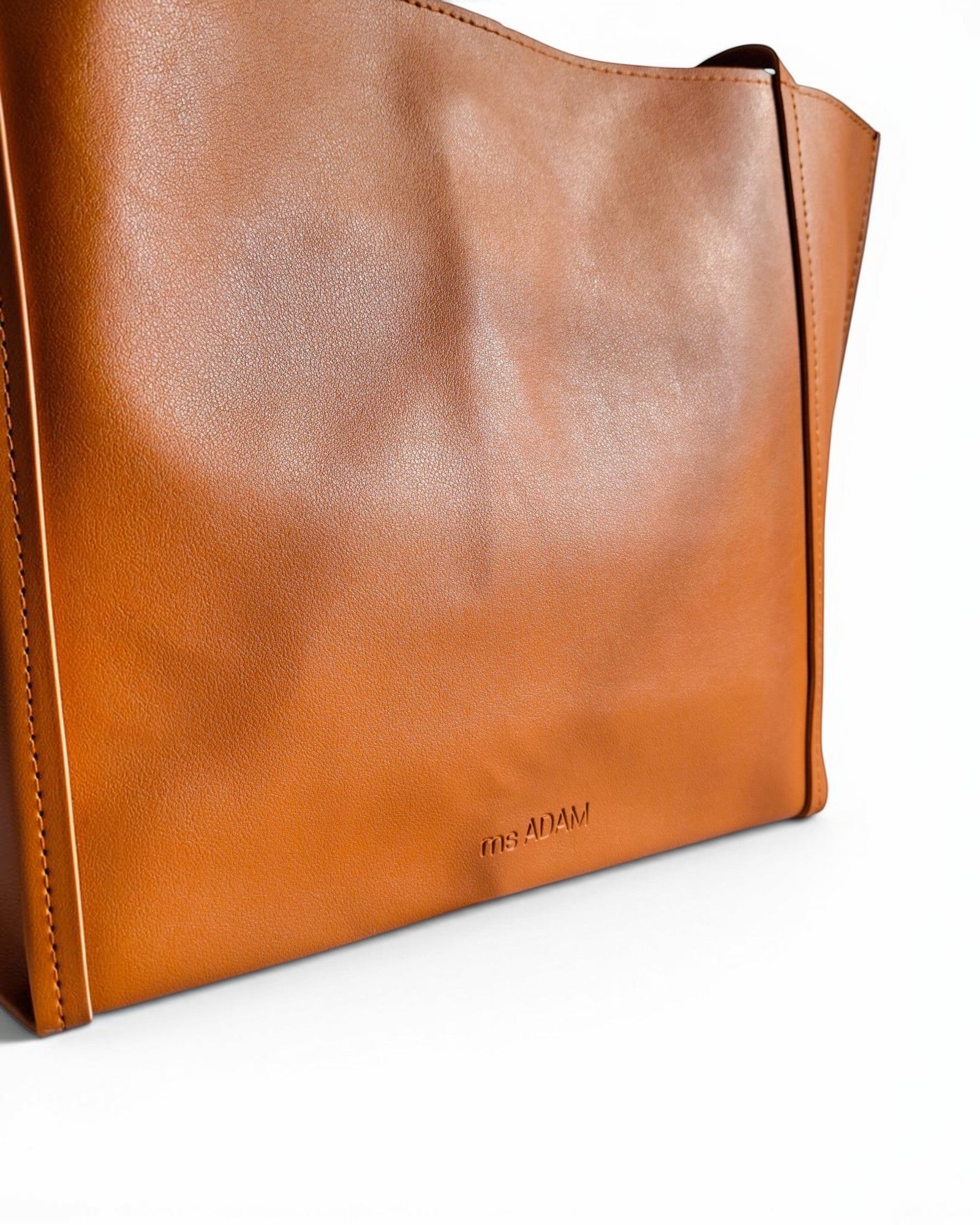 Ms Adam Go Easy Tote in brown faux leather. Spacious, unadorned tote with shoulder straps and magnetic snap closure.